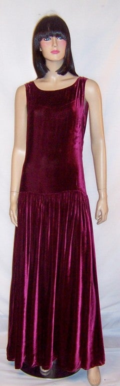 This is a luscious, deep red raspberry silk velvet, floor length, sleeveless gown with a series of snaps for closure on the left side, a dropped waist line, and a low scooped-out back.  The elongated bodice hugs the waist line and hips and the long