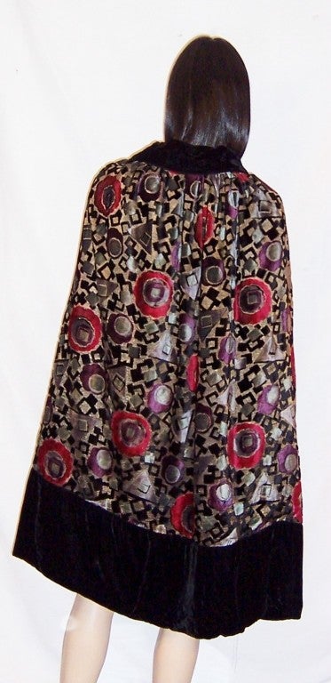 This is an exquisite 1920's vintage, cut-silk velvet and lame cape trimmed in black velvet. The color palette of black, steel gray, cerise, violet, and pale teal blue is unusual and captivating.  The cape has two long silk velvet sashes to be tied