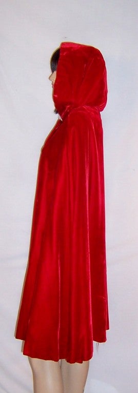 Offered for sale is this dramatic and vivid, cherry red velvet, hooded evening cape.  The cape has three lucite buttons encrusted with rhinestones for closure and a slit at either side for one's arms.  It is in excellent vintage condition, both