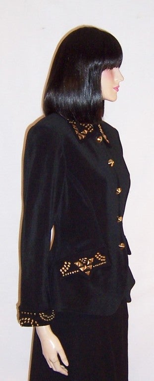 This is a fabulously designed black single-breasted jacket or blazer embellished with brass studs of varying sizes and shapes around each cuff, at each pocket, and around the collar. It is fully lined, masterfully constructed, form fitting and