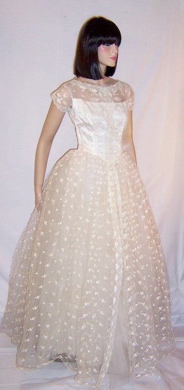 Offered for sale is this lovely and fanciful, 1950's vitnage, lace and embroidered tulle ball gown, possibly used as a debutante's cotillion ball gown or perhaps as a wedding gown. It has a satin lining, a semi-illusion top, capped sleeves, a fitted