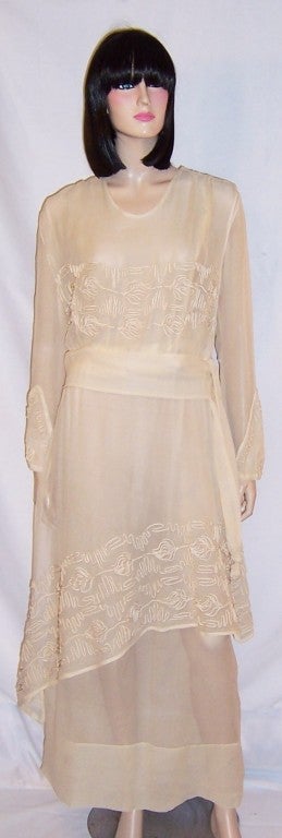 This is a lovely Edwardian, ivory silk chiffon tea gown probably dating to approximately 1910, heavily embellished with soutache in the Arts & Crafts style with a asymmetrical overskirt, a wide cummerbund and long streamers terminated with soutached