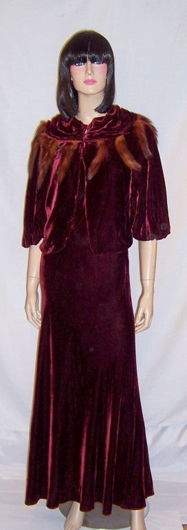 This is an extraordinary and sensuous 1930's vintage, deep burgundy silk velvet ensemble with a sleeveless gown, cut on the bias, and a matching bolero jacket with a ruched collar embellished with mink tails encircling its collar. The sleeveless