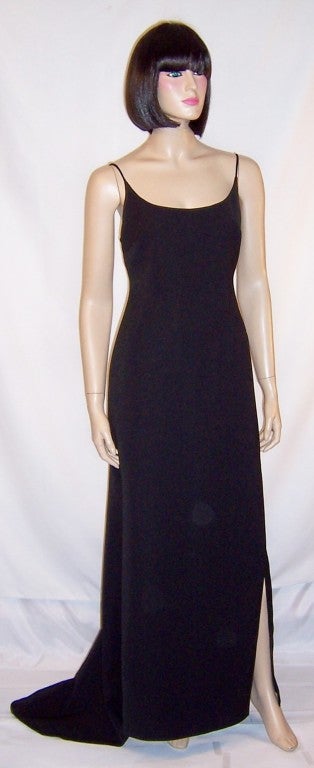 This is a simply elegant and unadorned Badgley Mischka black evening gown with a modified train. The gown has a scooped neckline, spaghetti straps, a slit up the left side of the gown to the knee, and a back zipper for closure. It is marked a Size 6