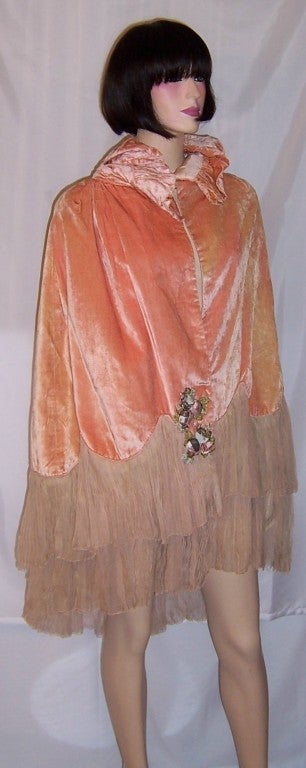 This is an exquisitely luxurious 1920's apricot velvet cape with pleated chiffon trim and a large bow at the back of the neck accentuated with a cluster of hand-made silk flowers.  A similar cluster of hand-made silk flowers appears at the front of