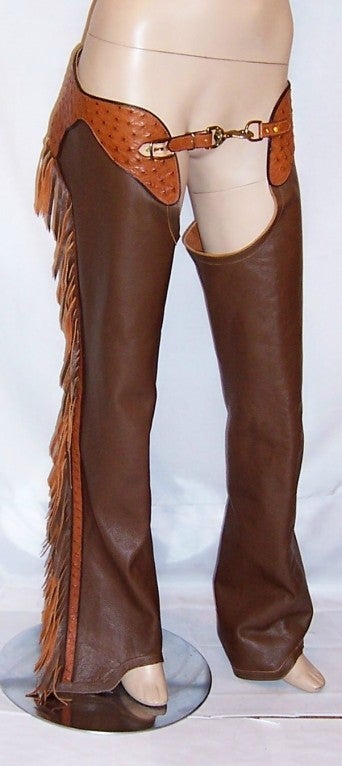 This is a fabulous pair of brown cowhide and deep ochre-colored ostrich leather chaps with zippers and  suede and leather fringe down each leg.  Chaps are sturdy leg coverings consisting of leggings and a belt. They are buckled on over trousers with