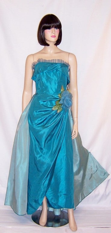 This is an exquisite and alluring, 1950's vintage, two-toned turquoise, taffeta, strapless gown with a fitted bodice trimmed with a tulle ruffle, a gracefully draped skirt with ruching accented with a large silk turquoise rose at the left hip, and a