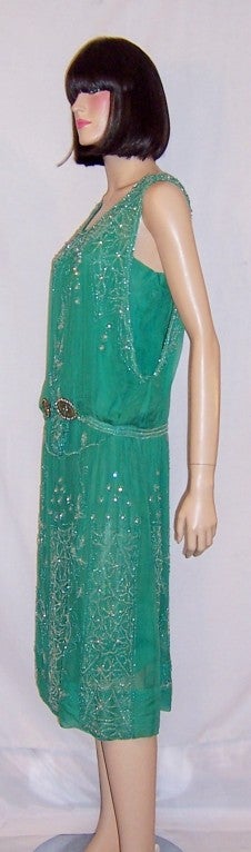 This is a spectacular 1920's vintage, viridian green beaded gown on chiffon with green and white beadwork designs accented with clear paste stones.  The gown is sleeveless with a dropped waist line and has its own silk slip attached. It must be