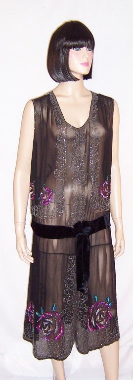 This is an exceptionally gorgeous 1920's Art Deco black chiffon beaded gown which has been embellished masterfully with orchid and pink stylized roses with green leaves in tiny sequins. The gown is sleeveless, with a scooped-out neckline, and a
