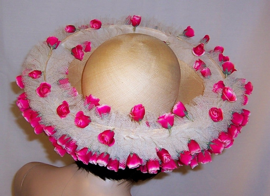 This is a gorgeous and fanciful custom-made, one-of-a-kind,  Jack McConnell creation,  whose interior and exterior brim is covered in white tulle  and is then embellished with bright pink rose buds encircling its crown. The crown's interior is