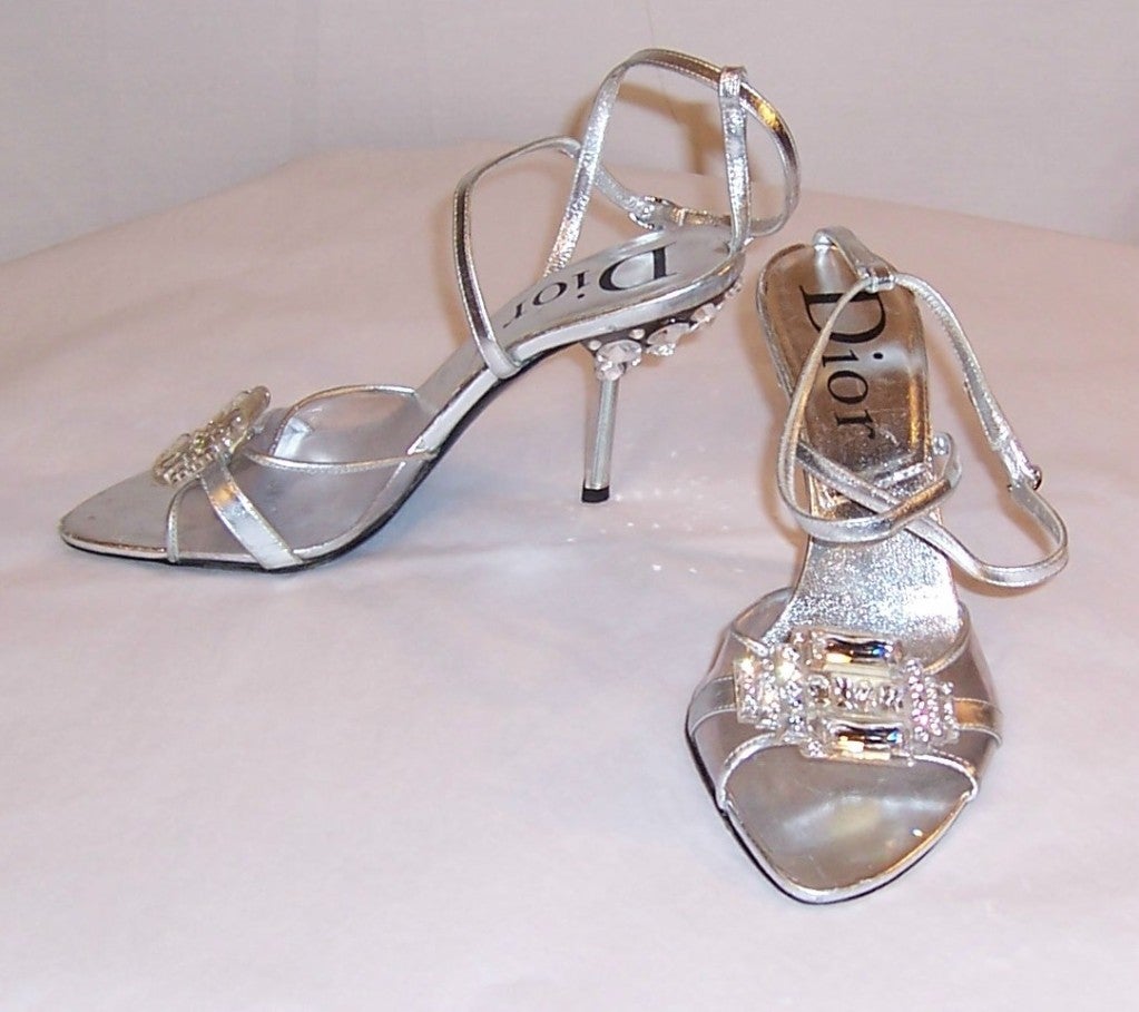 This is a wonderful pair of Christian Dior strappy silver evening shoes whose heels are encrusted with Swarovski crystals of varying sizes. The pair is  in very good to excellent vintage condition with the exception being that the  heel of the right