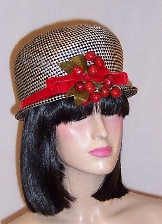 This is a delightful black and white checked straw topper  whose crown is encircled with red velvet ribbon and a bunch of bright red cherries, designed by Mr. John. The hat's circumference measures 22