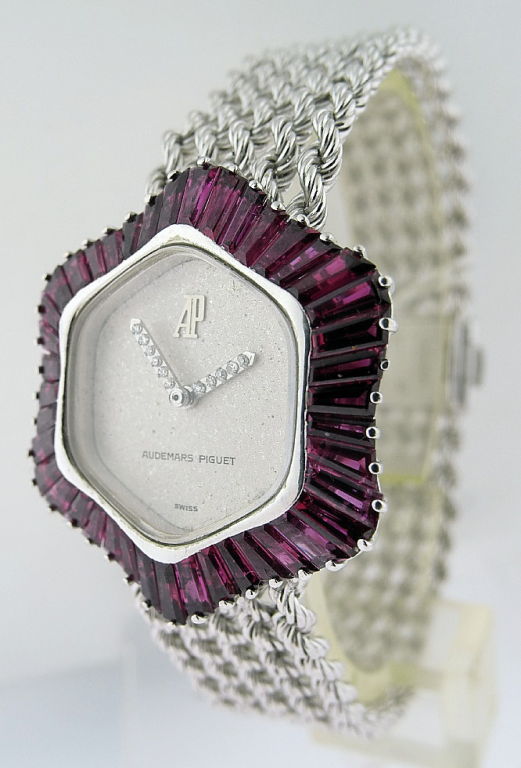 This is a Audemars Piguet, 18k white gold b-wind lady's bracelet wristwatch with 5ct baguette rubies and diamond hands. Manufactured circa 1990. Asymmetrical case #103780. Textured silver dial signed Audemars Piguet. Weight 46.1gr.
