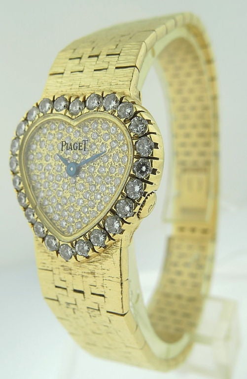 This is a Piaget, lady's 18k yellow gold & diamond set heart-shaped bracelet watch. • quartz movement • pavé-set diamond dial • 18k yellow gold heart-shaped case, diamond-set bezel • with an integrated 18k yellow gold bracelet and clasp • case,