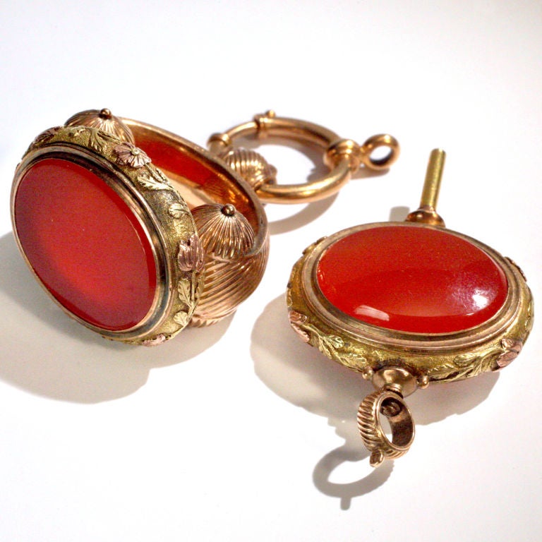 Striking antique watch fob set distinctly designed in a mixture of 14 karat yellow and rose gold.  The fob and the matching key with bezel cut vibrant colored carnelian stones.  Each piece with a ribbed pattern and delicate trailing flower design on