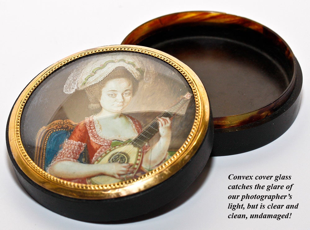 Exceptionally fine museum quality 1700s snuff box mounted with a fine portrait miniature showing a woman with mandolin and charming period costume, furnishings visible behind her. The painting is on ivory, and is mounted in 12k gold mounting ring