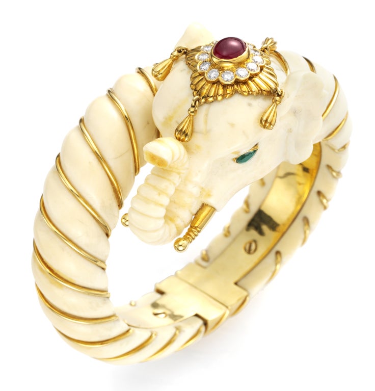 Van Cleef & Arpels, A Multi-Gem, Ivory and Gold Elephant Bangle, designed as a carved ivory elephant with pear-shaped emerald eyes, gold tusk, a headdress of gold, accented by a cabochon ruby and circular-cut diamond with gold tassels, to the