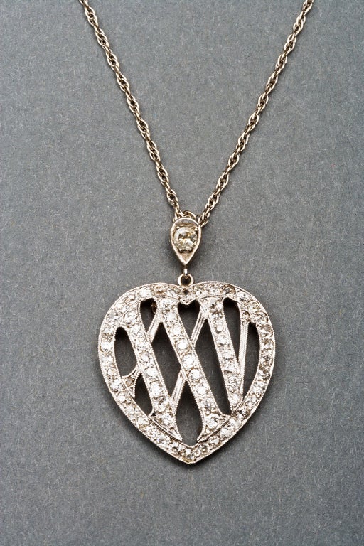 A beautiful 25th anniversary pendant, heart-shaped, the openwork Roman numerals XXV set with antique-cut diamonds, suspended from a diamond set bail, mounted in platinum-topped gold, attached to a white gold chain.

1 3/8 in. (3.5 cm.) long