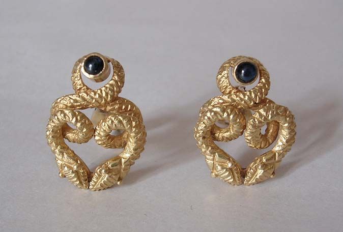 Designed as coiled gold serpents, each encircling a bezel-set deep blue cabochon sapphire. The serpent heads are accentuated with beaded gold eyes. Easy to wear, the textured 18k yellow gold earrings have a great look and good weight.  The earrings