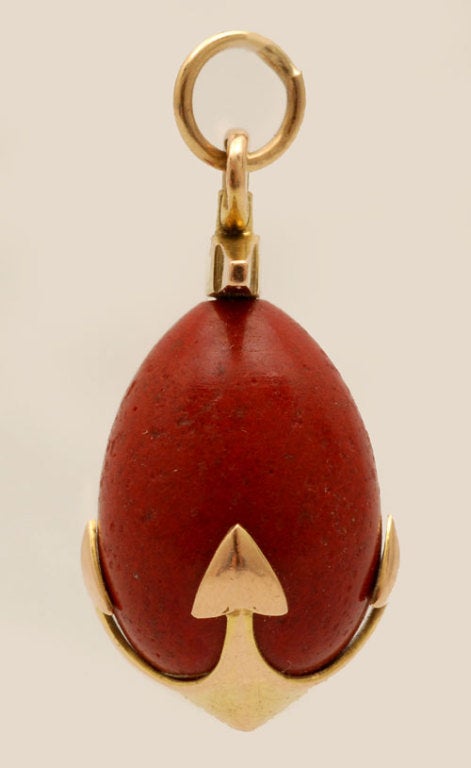 A Faberge gold mounted purpurine miniature pendant egg, ST Petersburg, circa 1908-17. The purpurine body decorated with a gold four-point anchor. Height: 1 1/8