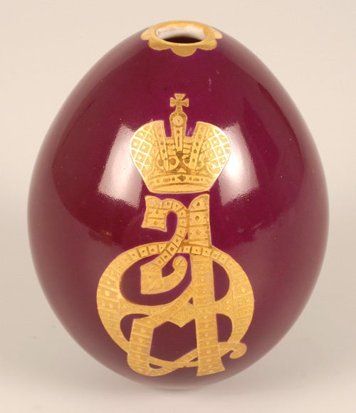 A Russian Imperial Presentation Easter egg, Imperial Porcelain Factory, Saint Petersburg, circa 1900. The deep red ground porcelain egg decorated with varicolor ciselé and embossed gilt cypher of Empress Alexandra Feodorovna surmounted by the