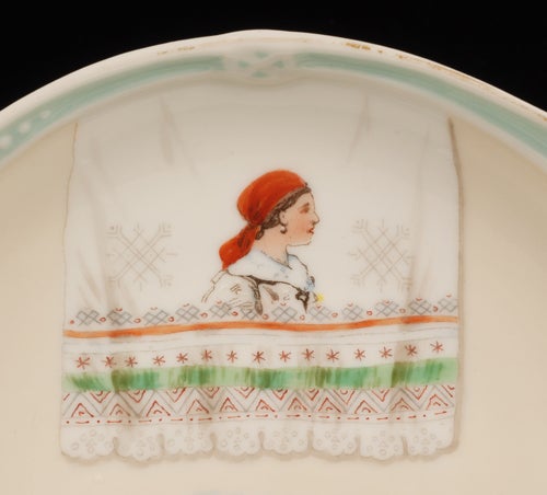 A low profile porcelain kovsh, Kornilov Factory, circa 1900. Of traditional form, the body decorated with a central image of a typical Russian barge beneath a painted polychrome trompe l’oeil linen towel, the shaped flat handle and prow decorated