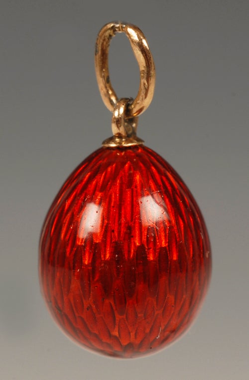 A Faberge gold and diamond mounted enamel miniature pendant egg, workmaster August Hollming, circa 1900. With strawberry red translucent enamel over an moire ground, set with a diamond. Height: 5/8