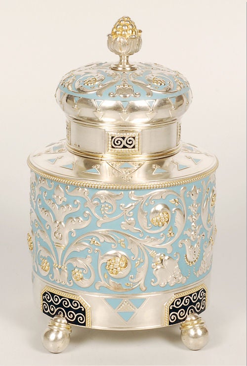 A large and impressive Fabergé silver, parcel-gilt, and enamel tea caddy, Moscow, 1908-1917. The body, of traditional cylindrical form on four ball feet, decorated with stylized scrolling repousse floral motifs against a pale blue opaque enamel