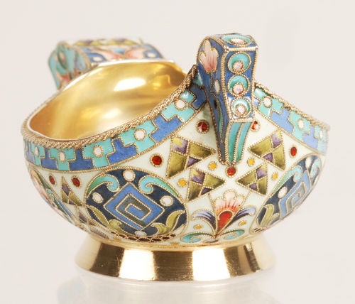 A Russian silver gilt and shaded cloisonne enamel kovsh, Ivan Khlebnikov, Moscow, circa 1908 - 1917. Of stylized form with a hook shaped handle and raised circular foot, the body enameled with multi-color geometric shapes against a cream ground.