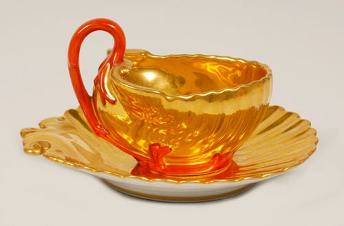 A Russian porcelain cup and saucer, Popov Factory, Moscow, mid 19th century. The cup formed as a scallop shell with gilded interior and molded sides with branching coral handle and base. The saucer decorated similarly. Height of cup: 3 1/4
