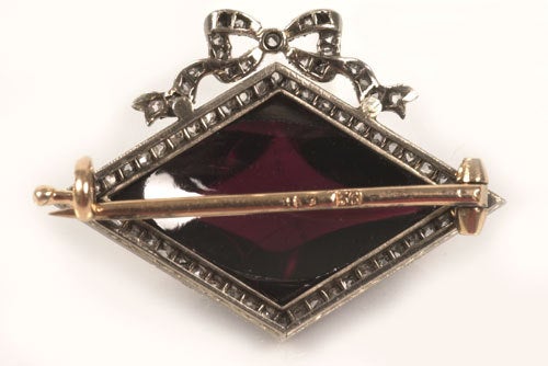 A Faberge gold and gem-set brooch, workmaster August Holmstrom, St Petersburg, circa 1900. Diamond shape cabochon garnet within a white gold frame and bowknot set with diamonds. Width: 1 1/8