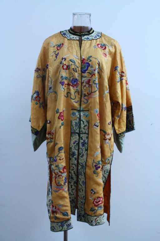 Post WWII Exotica peach robe with hand embroidered flowers and chinese motif in red, blue, pink and yellow. Chinese collar with black frogs for closure. Cuffs, collar and bottom are outlined in cream silk with vegetable-dyed flower embroidery. The