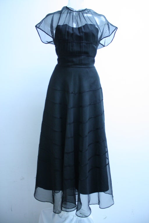 I place this dress in the late forties. It has magnificent  workmanship. It has a chiffon overlay with cap sleeves and a delicately rusched neckline. It features a longer tiered skirt. The sweetheart neckline is strapless. A very understated