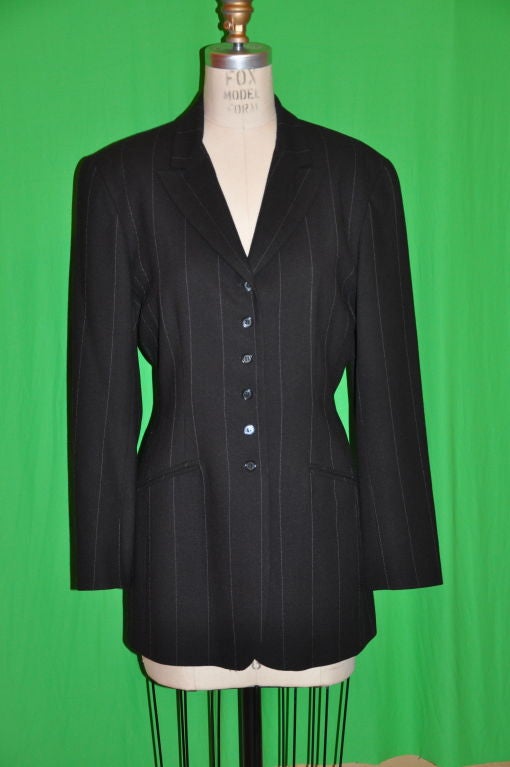 This Black wide pinstripe wool blazer has thin white pinstripes. The shoulders are lightly padded with two pockets in front. This six-buttoned blazer has four buttons detailing on the sleeves cuffs. The blazer has a fitted waist, unlike the usually