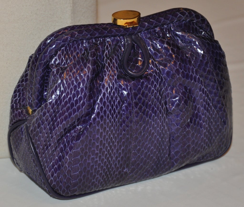 Die Saks Fifth Avenue Clutch in einem tiefvioletten Reptil-Ton hat optionale Schulterriemen, die im Inneren verstaut werden können. Rahmen und Verschluss aus goldenem Metall. Die Clutch ist an den Rändern mit Lederpaspeln verziert.
  Die Kupplung