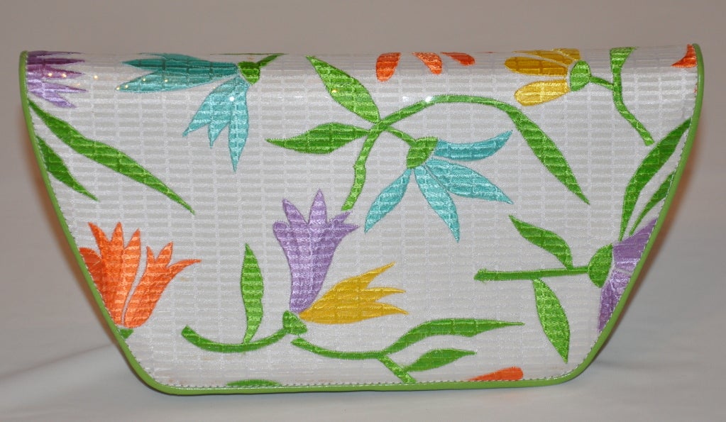 Charles Jourdan embroidered floral clutch is highlighted with clear strips over-lapping the hand-embroidery. The back and front of the clutch is over in bright lime-green calfskin. When opening the flap, the interior is lined in metallic silver