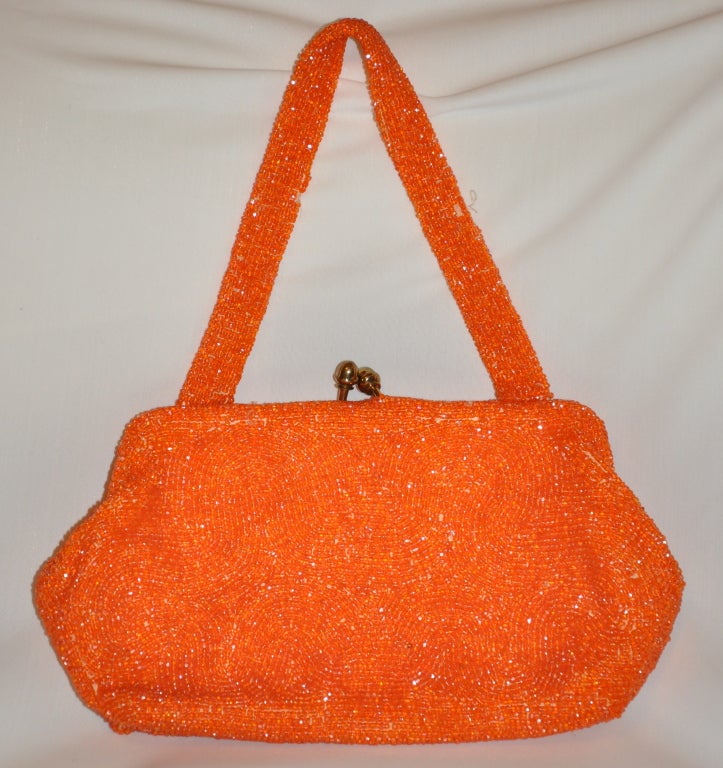 Die handgefertigte Abendtasche Bonwit Teller Tangerine besteht aus mikrokleinen Glasperlen, die in Wellen von Halbkreisen angeordnet sind. Der von Hand in Beligum gefertigte Rahmen mit goldenen Beschlägen wird durch eine ovale Öffnung mit