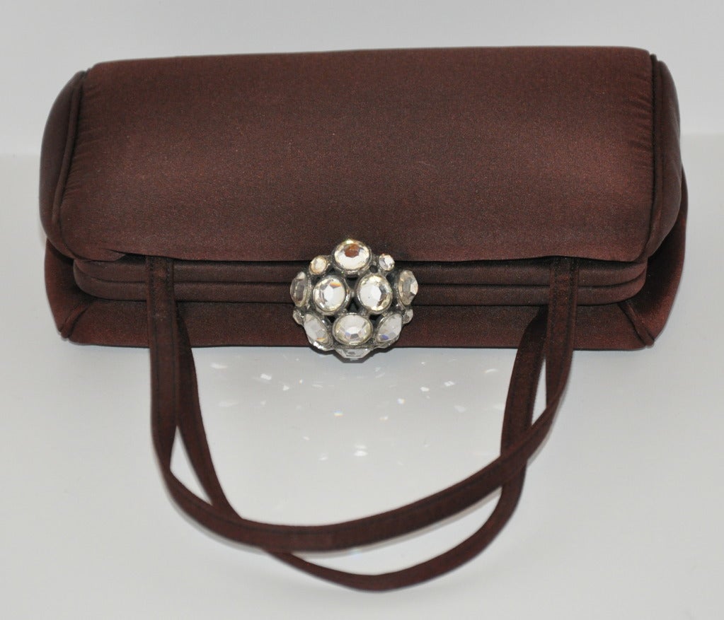 Ce sac à main miniature en satin de soie brun foncé est souligné par un grand fermoir incrusté de strass. Un magnifique passepoil en satin de soie est présent. L'intérieur est doublé de soie-satin avec un compartiment ouvert inclus. Les poignées