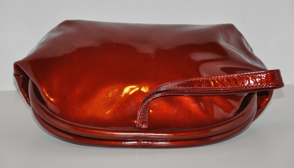 Cette pochette en cuir verni bordeaux-bronze de Ted Lapidus, merveilleusement réalisée, est dotée d'une poignée à l'arrière, si l'on veut la porter. Il y a une chaîne en or qui peut être utilisée comme sac à bandoulière si vous le souhaitez. Leur