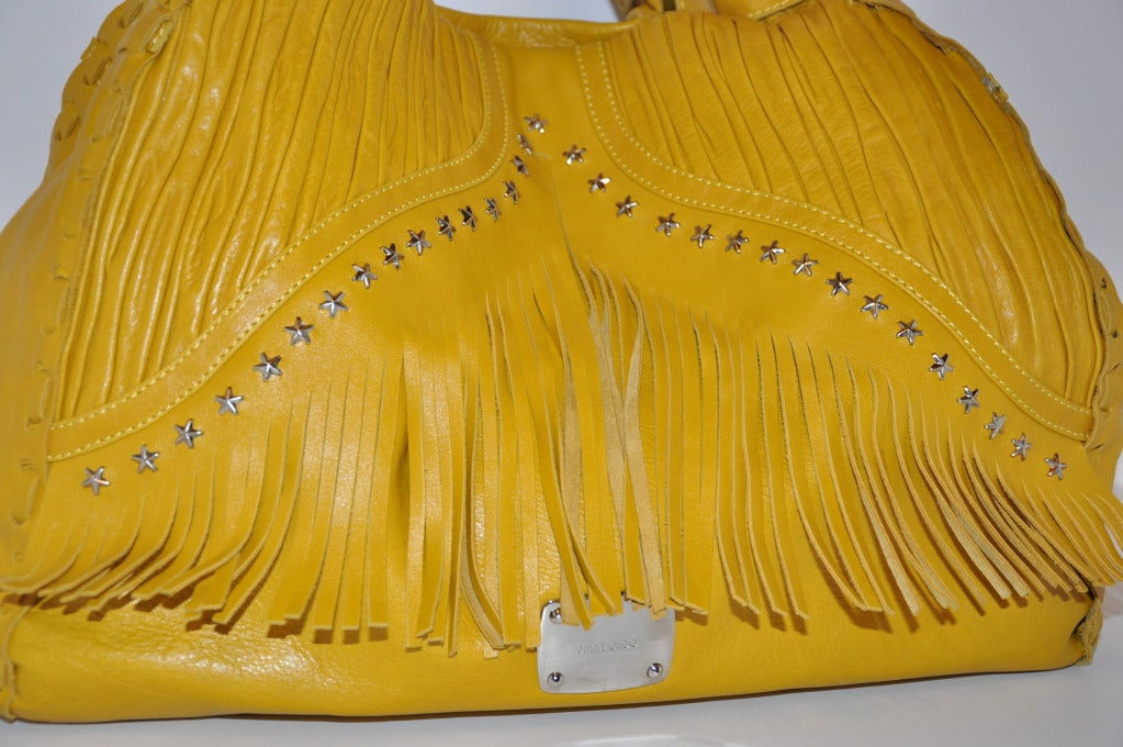 Jimmy Choo's Huge Banana-Yellow tote bag is accented with fringes and detailed with carefully folded lambskin on front along with embellished stars in gold hardware. Top-stitching is detailed throughout, as well as the hand-weave leather. 
   Bag