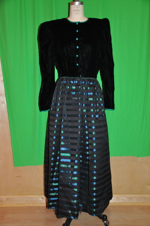 William Pearson velvet and silk Taffeta evening gown has a velvet long sleeve top and the skirt is of striped silk taffeta. The multi-colored striped skirt are in colors of violet, green, fuchsia, and black. There are seven (7) hidden snaps