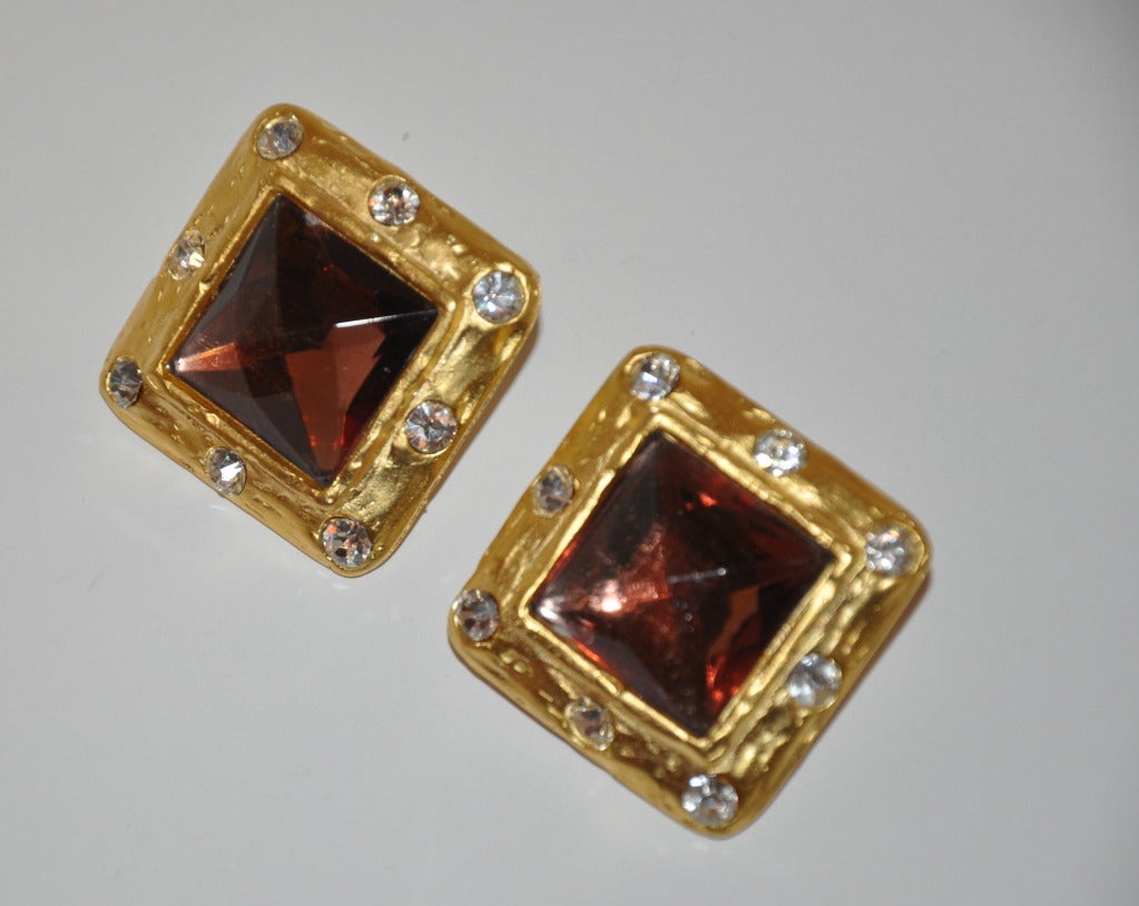 Ces grandes boucles d'oreilles à clip en or doré sont bordées de strass de couleur et centrées d'une grande pierre de verre colorée.            Les mesures sont de 1 1/16