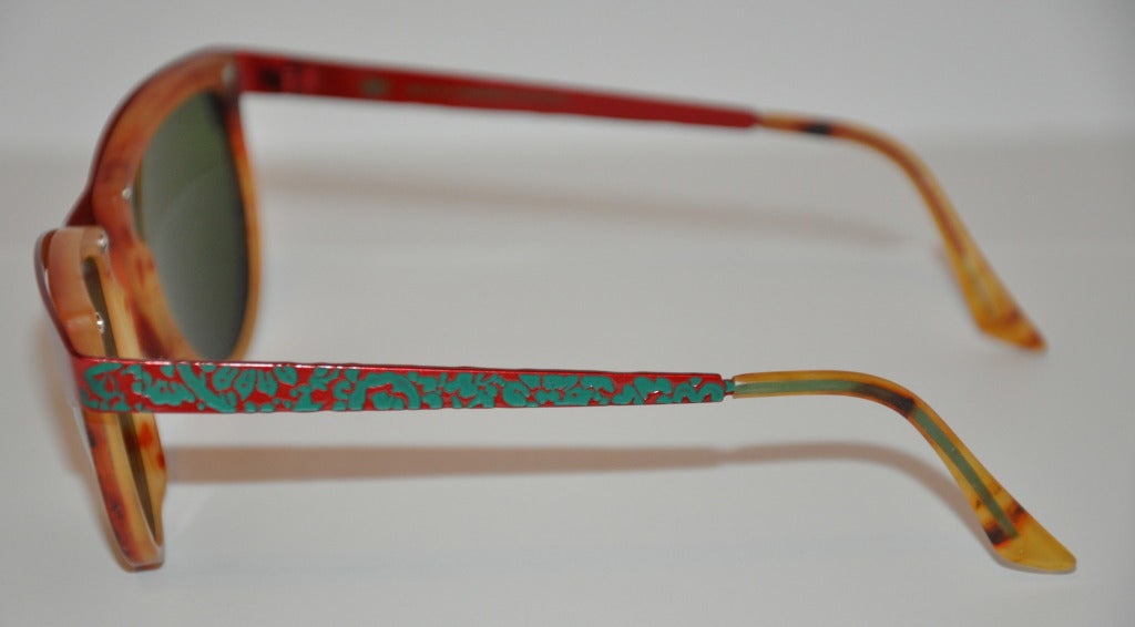 Oilily's wonderfully combination of textured red and green metal hardware frames are highlighted along with tortoise shell lucite around the front interior and finished with silver hardware nail studs. Extremely detailed in every way. The end-tips