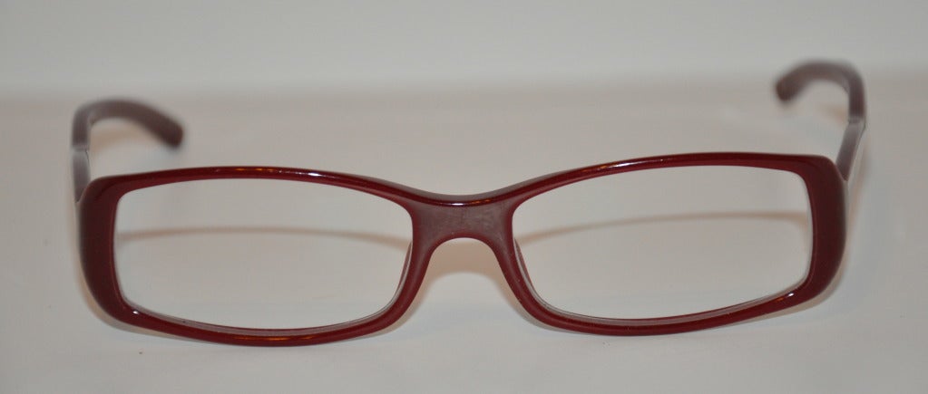 Prada brick-red lucite glasses have sides that are trimmed with silver hardware trim and accented with micro-size 