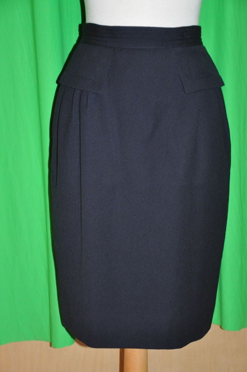 This Valentino black wool skirt is fully lined. There are three (3) small pleats underneath the two front flaps for detailing, and at the center back, a simple 