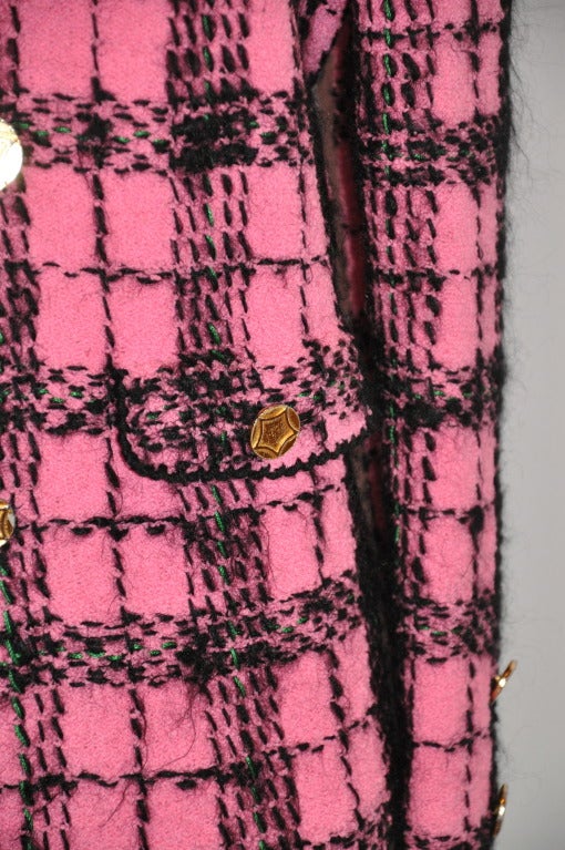 L'audacieuse veste à carreaux de laine fuchsia et noire d'Adolfo, entièrement doublée, comporte des boutons en métal doré sur le devant et aux poignets.
   Le devant mesure 18