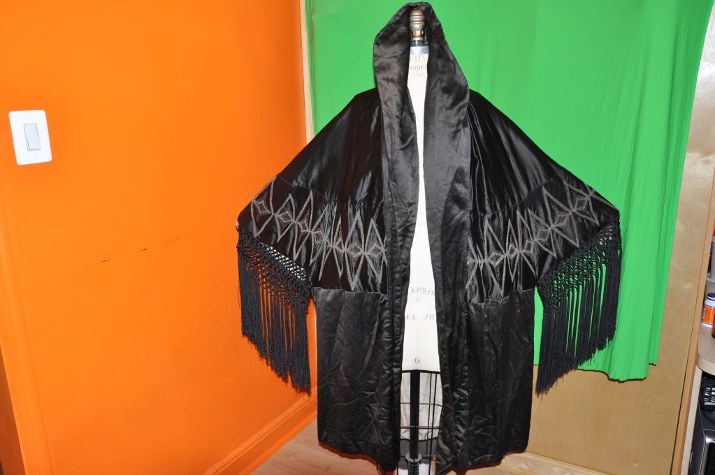 This spectacular Victorian black silk opera coat has hand-knotted fringes on the sleeves. The collar can be worn down, high and even as a hood. On the back center of the neckline, they are soft gathering and there are two darts, one on each back