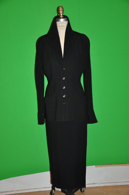 The jacket front has eleven (11) buttons on the front. Also, two breast pockets and two pockets on the bottom. The collar is a flat V neck with another lapel underneath giving the appearance of a blouse underneath a collarless jacket. The sleeves