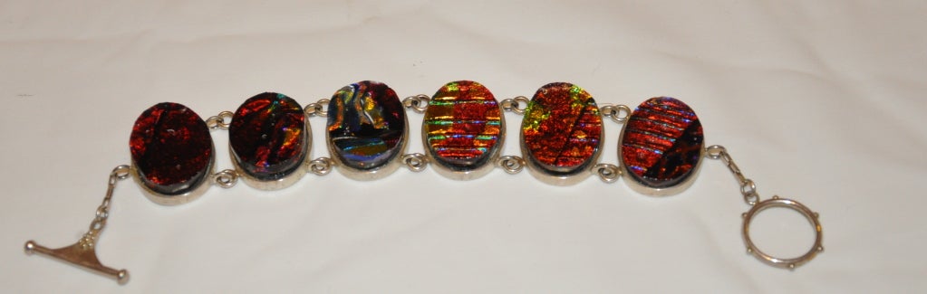 This rare Terika Blake Sterling Silver bracelet is set with iridescence poured glass in deep hues of reds, greens, yellows, and black. There are six links totally 8 5/8
