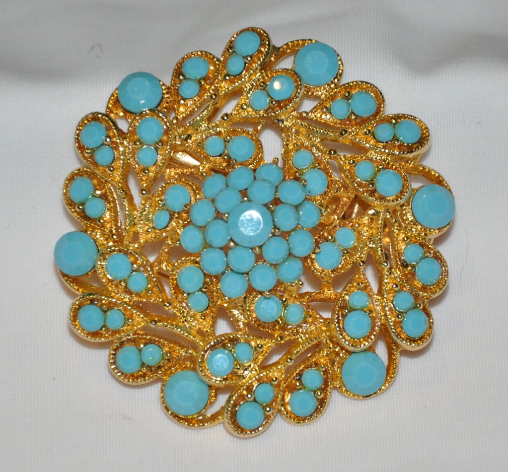 Diese Brosche mit vergoldeten Beschlägen ist mit türkisfarbenen Glassteinen in verschiedenen Größen in einem floralen Muster verziert. 
   Sie haben die Wahl, ob Sie sie als Brosche oder als Haarspange tragen möchten. Der Durchmesser ist 2 1/4